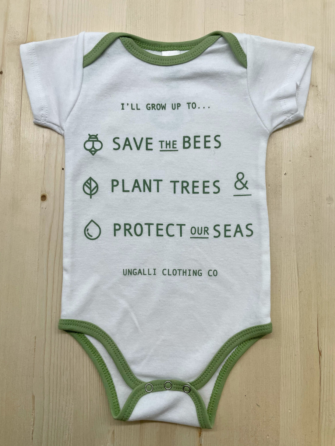 Babies organic onesie in white with green text that states: "Save the bees, plant trees & protect our seas"